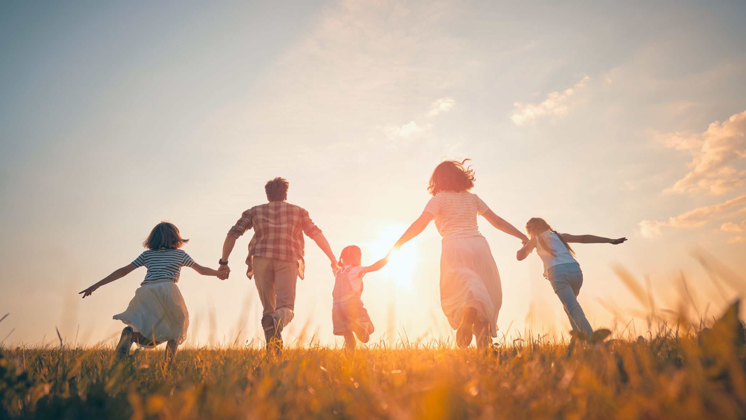 Una familia corre de la mano hacia el sol del atardecer